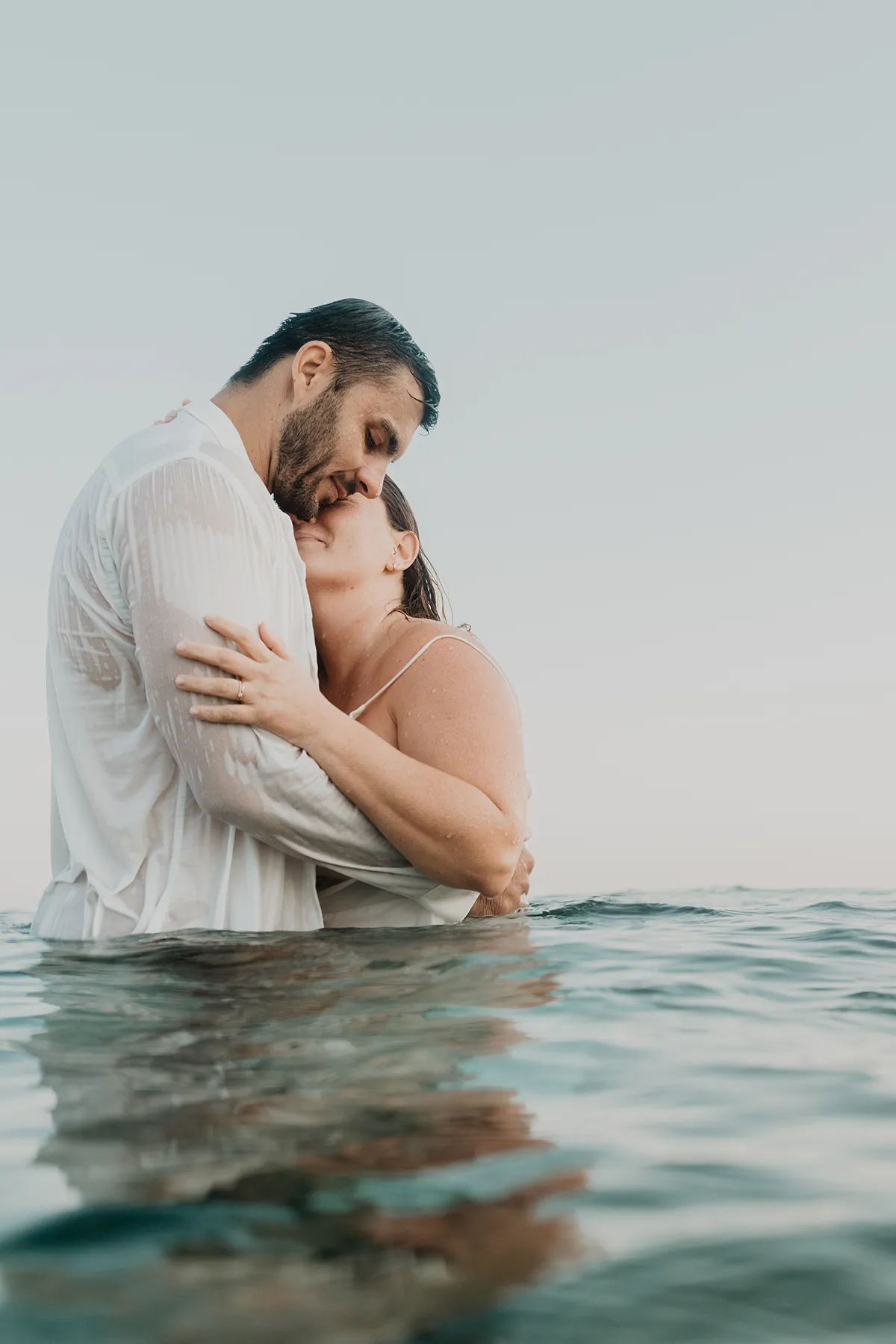 Mariée en robe posant sa tête sur le torse du marié en chemise blanche, mi-eau mi-air, Marseille