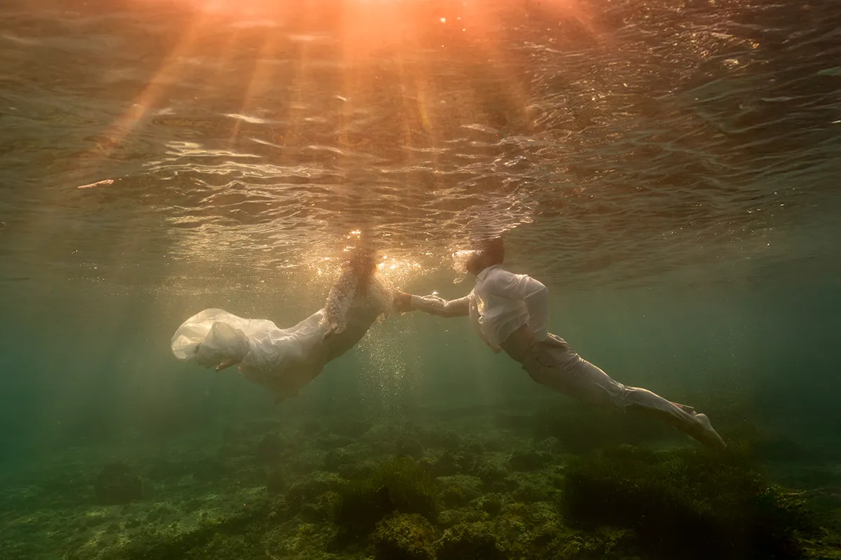 Couple de mariés se tenant la main sous l'eau, tête hors de l'eau, rayons de soleil, Marseille Calanques