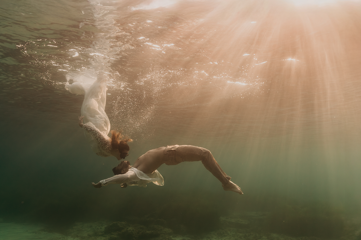 Plan large d'un couple de mariés flottant sous l'eau dans les Calanques de Marseille, robe de mariée déployée et décor sous-marin.