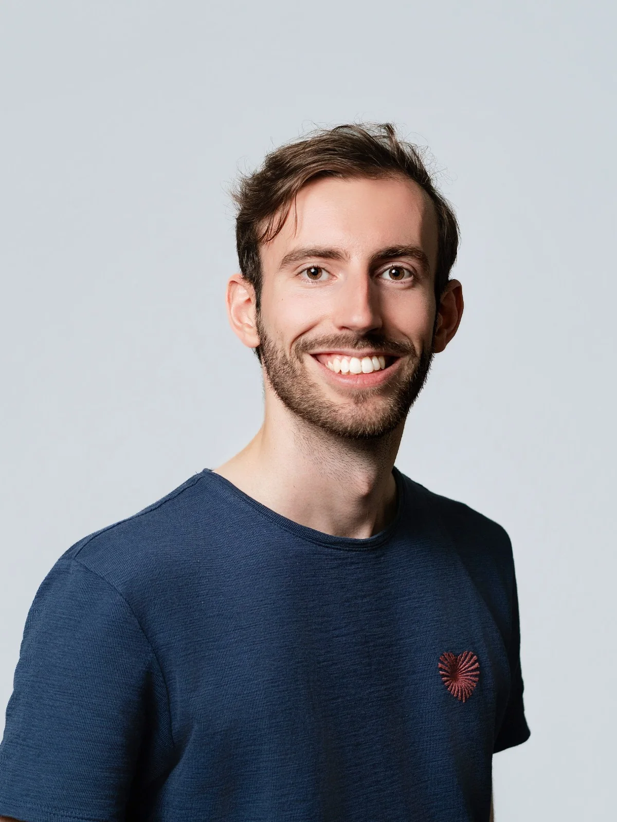 Portrait souriant sur fond gris, en tee-shirt bleu.