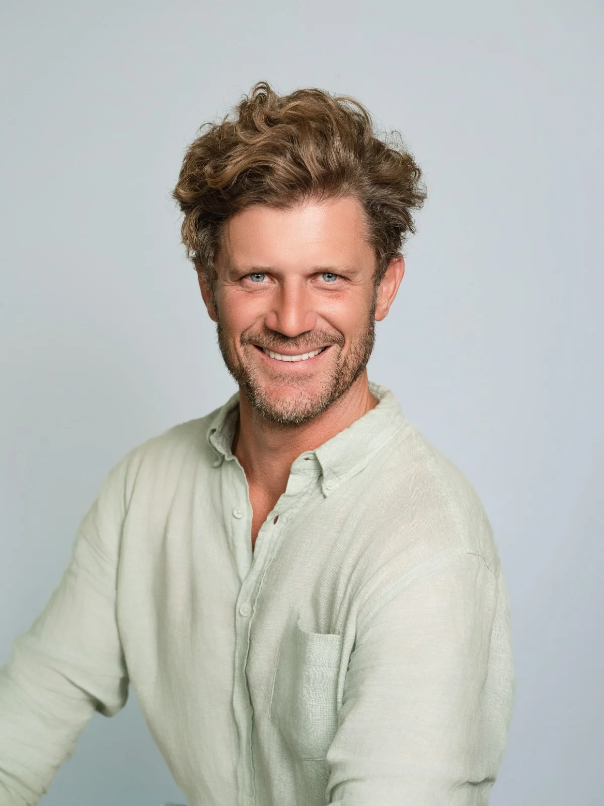Portrait souriant sur fond gris, en chemise claire.