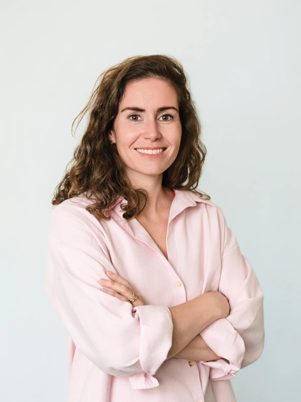 Portrait souriant sur fond gris, en chemise rose et bras croisés.